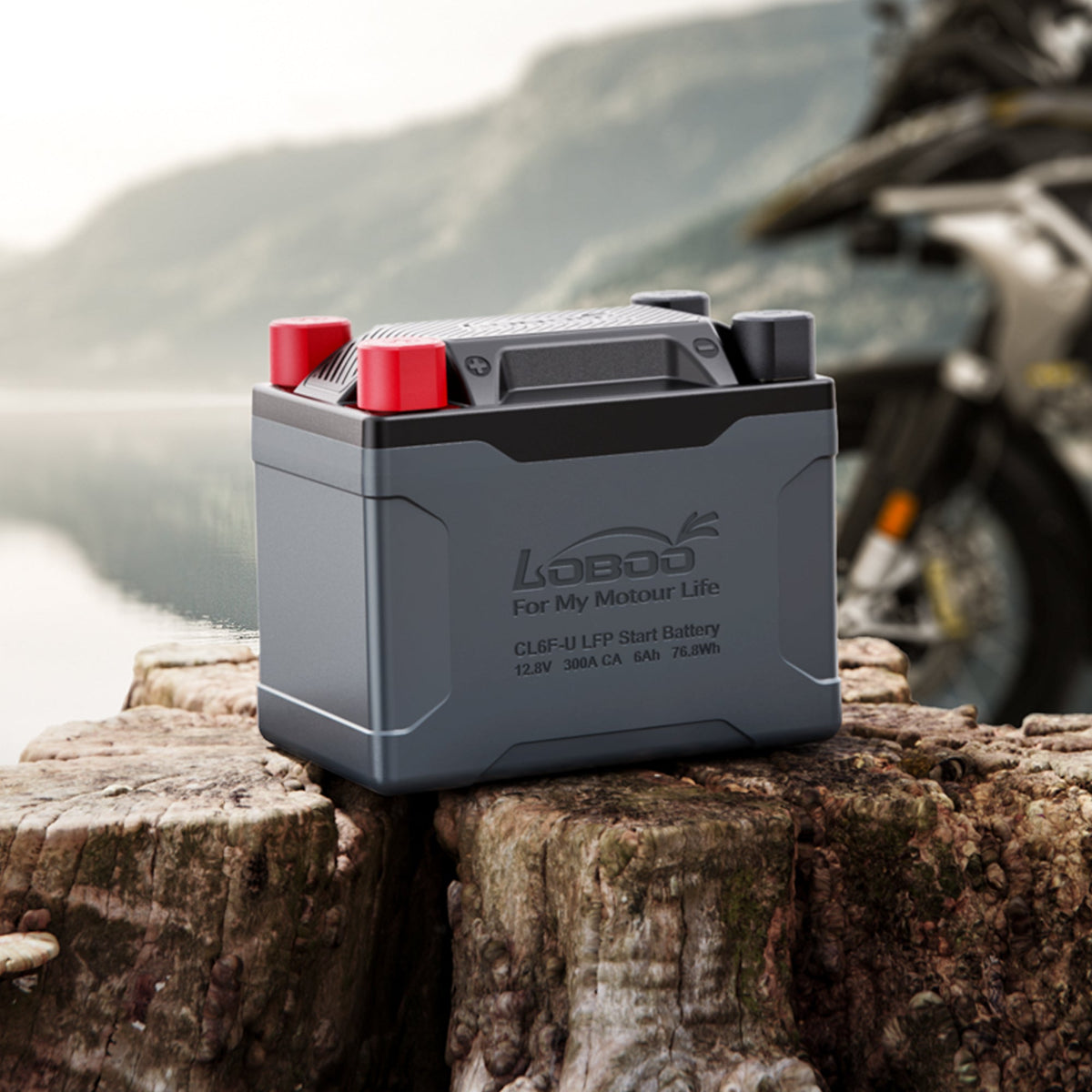 Batteria al litio LiFePO4 LOBOO appoggiata su un tronco con una moto adventure sullo sfondo